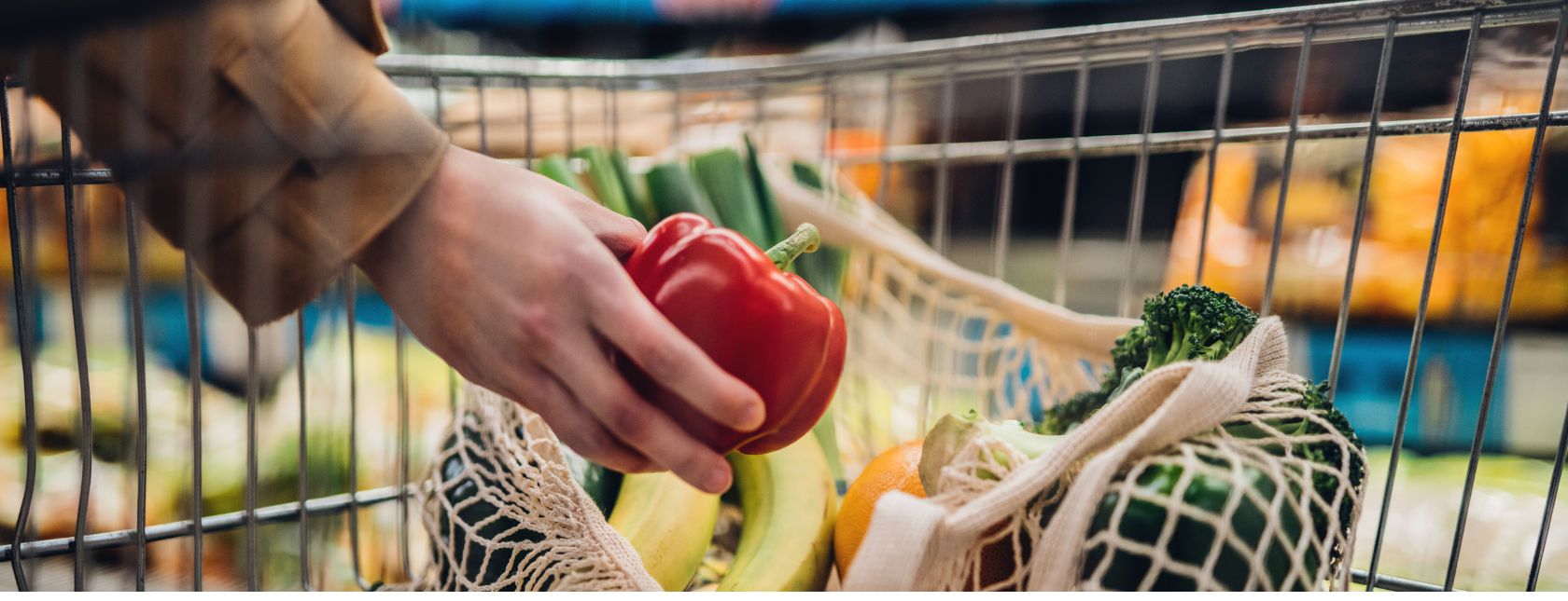 Female hand putting a red bell pepper into a mesh grocery bag